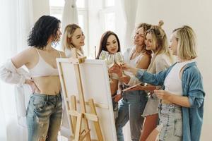 groep van Dames verf Aan canvas en drinken wit wijn gedurende partij Bij huis foto