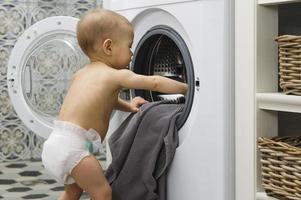 schattig baby jongen is op zoek binnen de het wassen machine foto