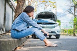 aziatische vrouw die naast de auto zit na een autopech op straat. concept van voertuigmotorprobleem of ongeval en noodhulp van professionele monteur foto