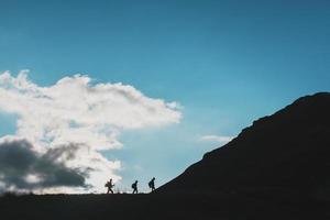 silhouetten van reizigers-toeristen beklimming bergop tegen de achtergrond van wolken en blauw lucht foto
