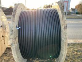 groot ronde houten spoelen van klossen met draden, zwart elektrisch kabels in rubber isolatie, gebruikt in de bedrading van geleider lijnen in industrieel bouw foto