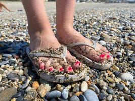 vrouw poten, voeten in rubber slippers met een mooi rood pedicure Aan de achtergrond van zand Aan vakantie Aan de strand in een warm tropisch oostelijk paradijs land zuidelijk toevlucht foto