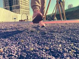 een jong mooi slank vrouw in een roze trainingspak en sportschoenen wandelingen Aan Purper stenen en grind in de sport- veld- in de binnenplaats van de huis foto