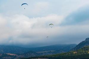paragliders paar Aan een achtergrond van wolken en bergen, drie paragliders foto