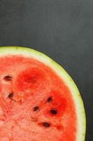 een rood arbukh is besnoeiing in voor de helft, Aan een zwart achtergrond, de structuur van sappig pulp van rijp rood watermeloen met zaden foto