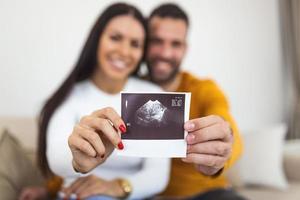 vrouw en haar vriendje Holding omhoog een beeld van haar echo van de baby. jong gelukkig paar met baby echografie foto