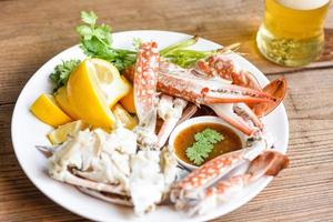 krab vlees met bier gekookt krab klauwen en poten Aan wit bord en zeevruchten saus Aan de tafel , blauw zwemmen krab foto