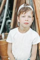 portret van een moe jongen zit leunend tegen de schuur deur met groen ogen. kind arbeid in de platteland foto