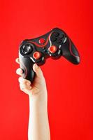 een kind hand- triomfantelijk houdt de gamepad Aan een rood achtergrond. foto