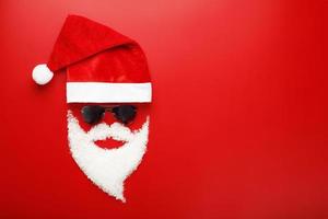 de kerstman claus hoed en baard gemaakt van sneeuw met zwart bril Aan rood achtergrond. foto