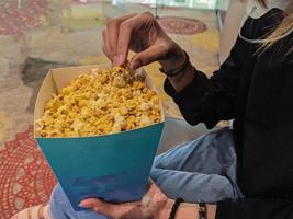 een jong vrouw eet zoet van smaak popcorn terwijl aan het wachten Bij de bioscoop foto