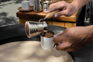 barista giet vers gemaakt Turks koffie in een beker, detailopname. een professioneel barista bereidt zich voor koffie door hand- in de traditioneel manier in de zand. selectief focus, ruimte voor tekst foto