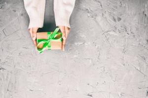 vrouw handen geven verpakt Valentijn of andere vakantie handgemaakt Cadeau in papier met groen lintje. Cadeau doos, decoratie van geschenk Aan wit cement tafel, top visie met kopiëren ruimte foto