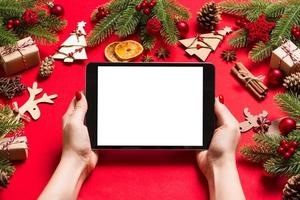 top visie van vrouw Holding tablet in haar handen Aan rood achtergrond gemaakt van Kerstmis decoraties. nieuw jaar vakantie concept. mockup foto