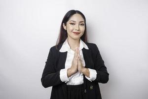 een glimlachen jong Aziatisch vrouw werknemer vervelend een zwart pak gebaren een traditioneel groet geïsoleerd over- wit achtergrond foto