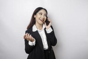 een portret van een gelukkig Aziatisch zakenvrouw is glimlachen terwijl pratend Aan telefoon telefoontje vervelend een zwart pak geïsoleerd door een wit achtergrond foto