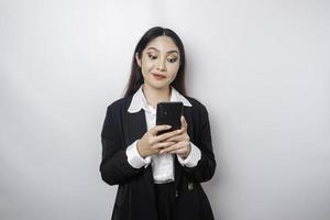 een portret van een gelukkig Aziatisch zakenvrouw is glimlachen en Holding haar smartphone vervelend een zwart pak geïsoleerd door een wit achtergrond foto