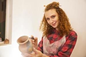 mooi curly-haired meisje lachend tijdens het schilderen van een vaas foto