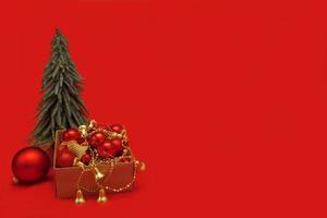 Kerstmis speelgoed in een doos in de buurt de Kerstmis boom Aan een rood achtergrond met kopiëren ruimte, Kerstmis inhoud foto