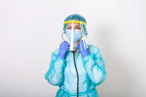 dokter, verpleegster tonen hoe naar vervelend bescherming pak voor vechten covid-19 corona virus met wit achtergrond geïsoleerd. medisch arbeider in vol beschermend uitrusting met gezicht schild zetten Aan haar stethoscoop