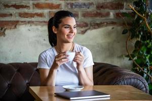 mooi jong vrouw met kop van koffie. vrouw geniet vers koffie in de ochtend- met zonsopkomst Bij koffie winkel mooi vrouw drinken koffie in de ochtend- zittend door de venster foto