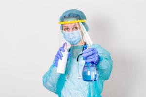 vrouw vervelend handschoenen, biohazard beschermend pak, gezicht schild en masker met hand- ontsmettingsmiddel fles en ontsmetting gel. corona virus of covid-19 bescherming. foto