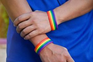 regenboog vlag holing in hand- van Aziatisch homo welke draagt regenboog polsbandje naar telefoontje uit en shows lgbt geslacht verscheidenheid en met inachtneming van geslacht alternatief in de omgeving van de wereld. foto