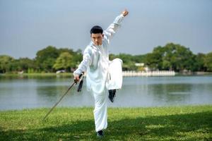 jong Mens beoefenen traditioneel tai chi zwaard, tai ji in de park voor gezond, traditioneel Chinese krijgshaftig kunsten concept Aan natuurlijk achtergrond . foto
