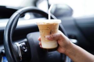 Bangkok, Thailand - mei 15, 2022 Aziatisch vrouw bestuurder houden ijs koffie kop voor drinken in auto, gevaarlijk en risico een ongeluk. foto