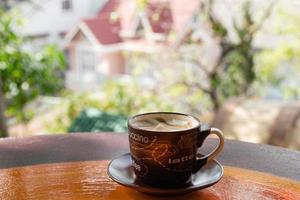 kop met heet melk koffie Aan een kleurrijk houten kleurrijk tafel in een cafe Aan achtergrond van stad visie. dalat, Vietnam. foto