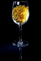 rauw pasta in glas kan, wijn glas. in emmer. rauw pasta Aan zwart achtergrond. voorkant visie rauw pasta, liet vallen van hand, plaats voor tekst, geel lang spaghetti rietjes, foto