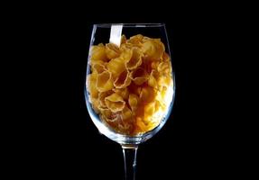 rauw pasta in glas kan, wijn glas. in emmer. rauw pasta Aan zwart achtergrond. voorkant visie rauw pasta, liet vallen van hand, plaats voor tekst, geel lang spaghetti rietjes, foto