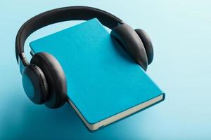 hoofdtelefoons zijn versleten Aan een boek in een blauw hardcover Aan een blauw achtergrond, top visie. foto