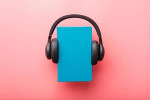 hoofdtelefoons zijn versleten Aan een boek in een blauw hardcover Aan een roze achtergrond, top visie. foto