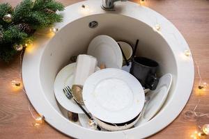 vuil gerechten in de wastafel in de met bloemenkrans keuken, een vakantie na een feest Bij kerstmis. knoeien na de gasten voor de nieuw jaar, keuken schoonmaak, wasmiddel, schoonmaak Diensten foto