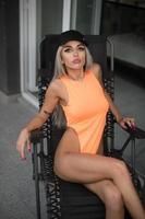 mooi perfect vrouw in oranje bodysuit poseren in voorkant van camera .aantrekkelijk slank blond met perfect gebruind lichaam gesteld in balkon. foto