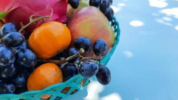 dichtbij omhoog, tropisch draak fruit sinaasappelen, peren, druiven in een groen mand Aan een wit achtergrond 04 foto