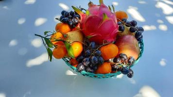 hoog hoek, tropisch draak fruit sinaasappelen, peren, druiven in groen mand Aan wit achtergrond 02 foto