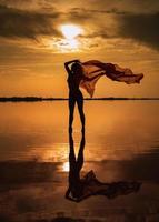 silhouet van een meisje in een rood zwempak Aan de strand. rood zakdoek ontwikkelt in haar handen. foto