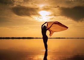 silhouet van een meisje in een rood zwempak Aan de strand. rood zakdoek ontwikkelt in haar handen. foto