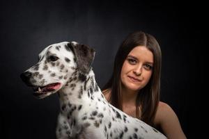 een jong mooi vrouw is spelen met haar dalmatiër huisdier, geïsoleerd Aan een zwart achtergrond. foto