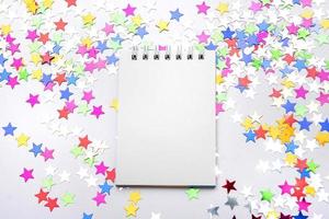 wit notitieboekje Aan een wit achtergrond met verspreide veelkleurig schitteren sterren. plaats voor tekst foto