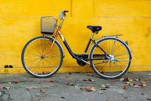 oud fiets Aan een achtergrond van helder geschilderd geel muur en herfst bladeren Aan een straat. foto