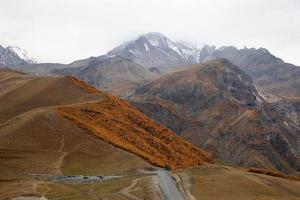 weg in de bergen in herfst tijd Aan een achtergrond van Kaukasus bergen met besneeuwd piek, Georgië. foto