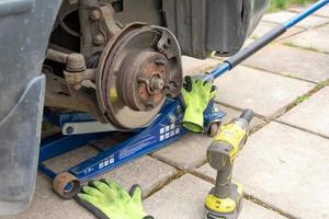 de voorkant schijf rem en een deel van de voorkant suspensie Aan de auto zijn in de werkwijze van inspectie en vervanging. de auto is opgevijzeld omhoog, de rem schijf en de remklauw zijn zichtbaar. foto