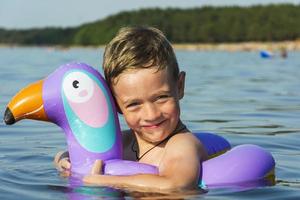 schattig jongen met een opblaasbaar zwemmen cirkel in de het formulier van een toekan zwemt in de blauw water van de zee foto