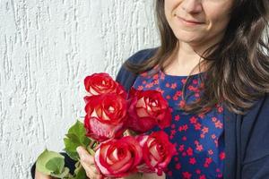 de meisje is Holding een boeket van rood rozen Aan een licht achtergrond. kopiëren ruimte. een geschenk voor Valentijnsdag dag, verjaardag. moeder dag foto