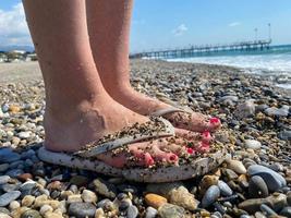 vrouw poten, voeten in rubber slippers met een mooi rood pedicure Aan de achtergrond van zand Aan vakantie Aan de strand in een warm tropisch oostelijk paradijs land zuidelijk toevlucht foto