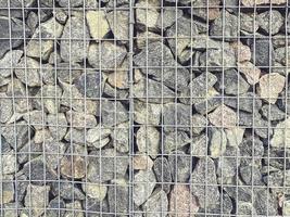 stenen in een metaal gaas. een berg van grijs, volumineus, structureel stenen liggen in een metaal structuur net zo een element van decor. diy hek voor huis foto