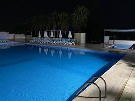 mooi nacht zwemmen zwembad met paraplu's en dek stoelen en palm bomen in een hotel Aan vakantie in een toerist warm tropisch oostelijk land zuidelijk toevlucht foto